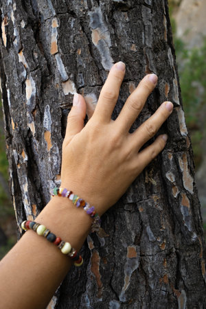 hand touching tree bark with colorful beaded bracelets in natureの写真素材