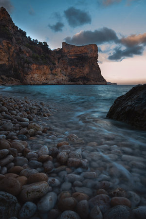 The rock rises above the blue sea in the orange rays of the setting sun against the background of the blue skyの写真素材
