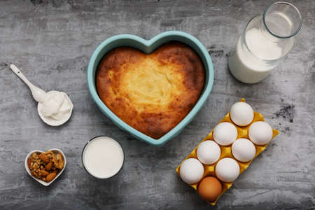 Heart-shaped casserole and ingredients on concrete.
