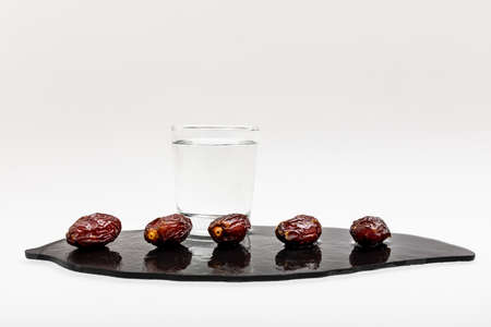 Five beautiful dates and a glass of clear water on a black stone. the horizontal frame.の写真素材