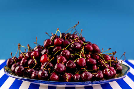 Fresh ripe maroon cherries on a huge earthenware dish on a blue-and-white striped table.