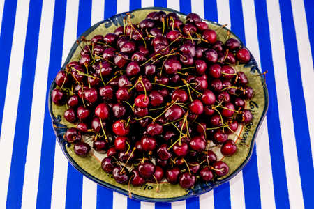 A large earthenware dish with ripe maroon cherries on a blue-and-white striped background.