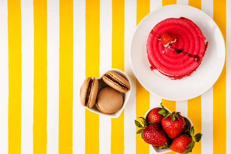 Chocolate macaroni cake, raspberry cake, fresh strawberries on a white and yellow striped background.の写真素材