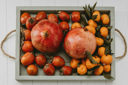tray with pomegranates, tangerines and persimmons on a light background