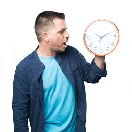 Young man wearing a blue outfit. Holding a clock. Looking surprised.