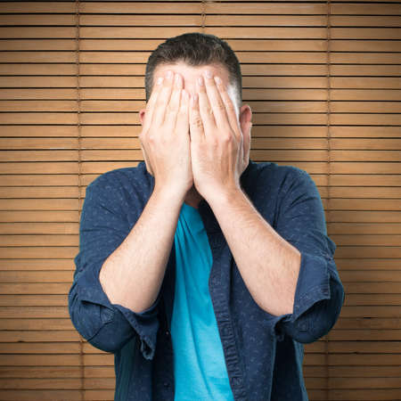 Young man wearing a blue outfit. Covering his face with his hands.の写真素材