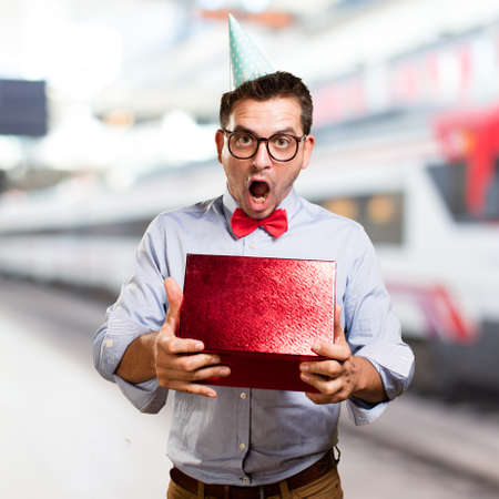 Man wearing a red bow tie and party hat. Holding gift. Looking surprised.の写真素材