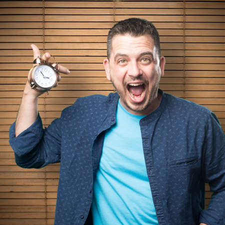 Young man wearing a blue outfit. Holding a clock. He is yelling.