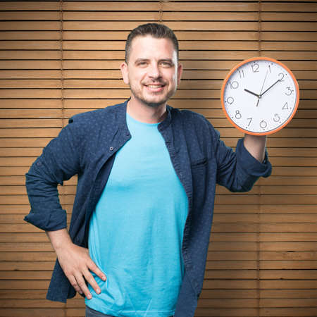 Young man wearing a blue outfit. Holding a clock. Smiling.