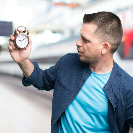Young man wearing a blue outfit. Holding a clock. Looking to it.の写真素材