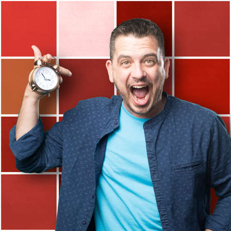 Young man wearing a blue outfit. Holding a clock. He is yelling.の写真素材