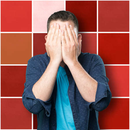 Young man wearing a blue outfit. Covering his face with his hands.