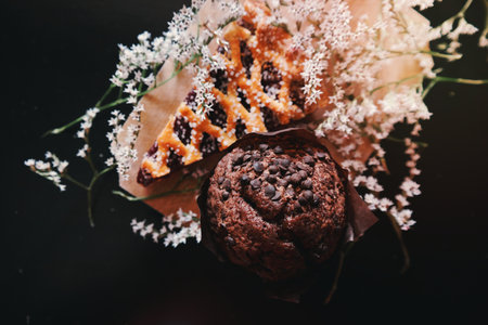 An overhead shot of a chocolate chip muffin next to a piece of pie decorated with elderflowers.の写真素材