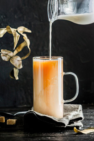 a glass of orange juice on a dark table with a pitcher pouring milk into it