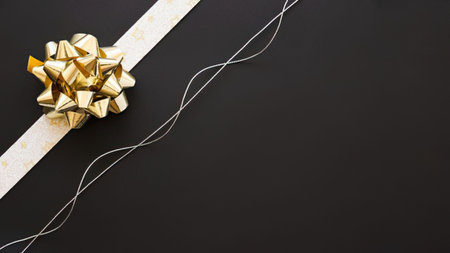 a gold bow sits on a white ribbon that stretches diagonally across a black background with a few strands of string to the right of the ribbon