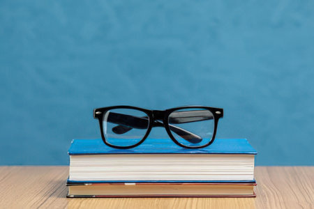a stack of books with a pair of black glasses on top, sitting on a wooden table against a blue wall