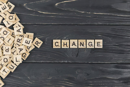 a collection of wooden scrabble tiles arranged to spell out the word change on a dark wooden surface with additional tiles scattered to the left