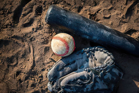 a baseball, a baseball glove and a bat on sandy ground with footprints