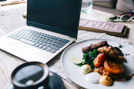 Laptop on the wooden table with a cup of coffee and salad