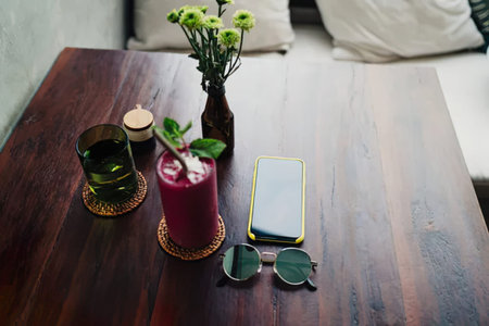 Smartphone with red smoothie and sunglasses on the wooden table.