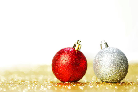 Two festive Christmas ornaments, one red and one silver, on a glittery gold surface with sparkles.