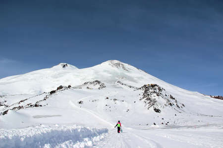 girl in a colorful suit with a snowboard is on the mountain roadの写真素材