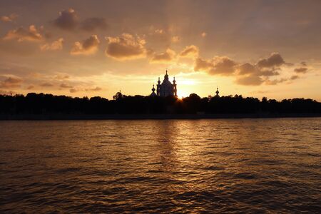 orange sunset over the river Neva with dark church silhouetted on the horizonの写真素材