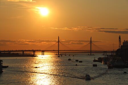 orange sunset over the river with a big bridge and boatsの写真素材