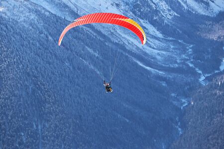 paraplane flying over snowy Caucasus mountains and sunny blue skyの写真素材