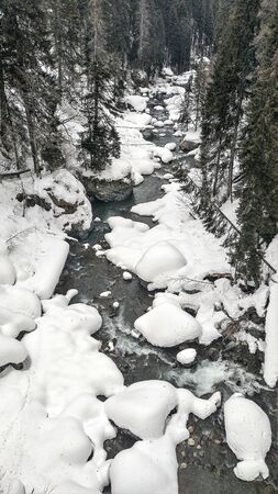 mountain river flows among the rocks and puffy white snow on the banksの写真素材