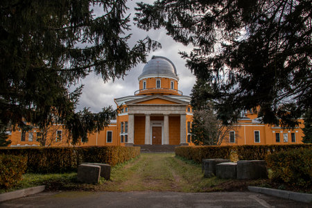 orange observatory building behind spruce trees in parkの写真素材