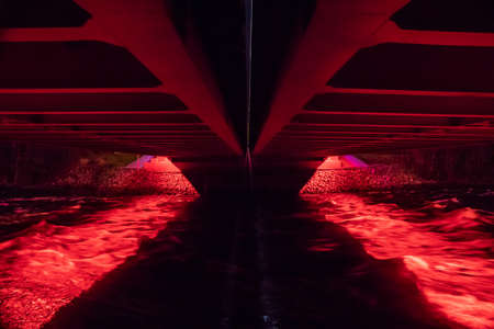 under a red illuminated bridge over a turbulent river rapids