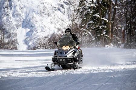 black snowmobile rides on a snowy road in the mountainsの写真素材