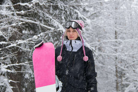 Girl with a snowboard in the forest in the mountains and the snowfallの写真素材