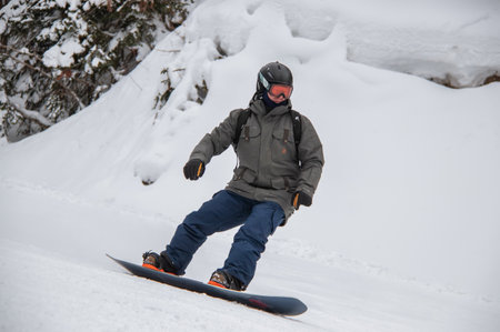 Man on a snowboard rides down the side of the mountainの写真素材