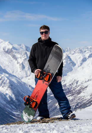 Portrait of a man with snowboard on top of a snowy mountain.の写真素材