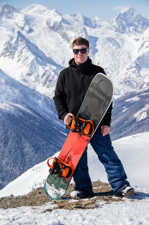 Portrait of a man with snowboard on top of a snowy mountain.の写真素材