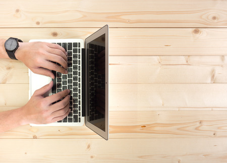 Male hands working on a laptop on a wooden desktop with copy spaceの写真素材