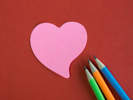 Pink heart-shaped memorandum on red paper with colorful pencils (remember meaning of love)の写真素材