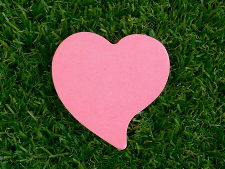 Pink heart-shaped notpad on green artificial grassの写真素材