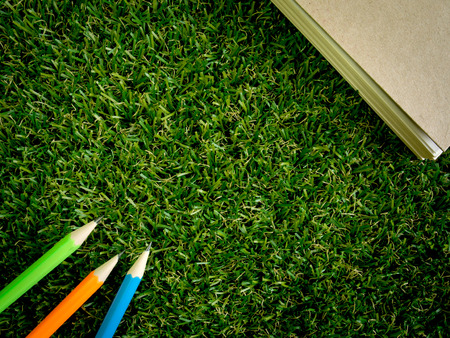 Book and colorful pencil on green artificial grass with copy spaceの写真素材