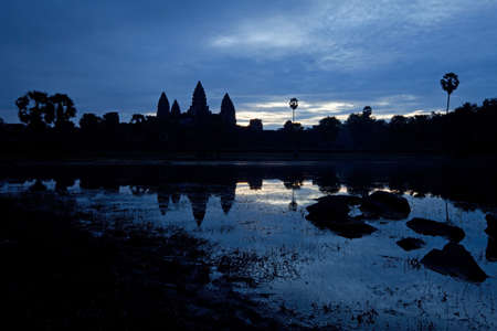 Silhouette of Angkor Wat complex at sunrise against dark blue sky 