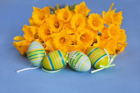 Painted Easter eggs with striped pattern and bunch of yellow daffodils on blue background 