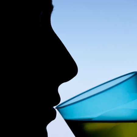 silhouette of a womans face, drinking green liquid from a transparent blue glass 