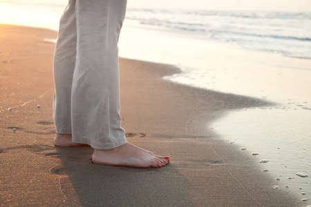 Barefoot woman on the golden sands of a beach in the sunset の写真素材