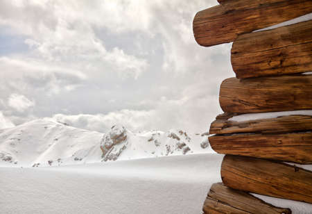 Snow covered wooden cabin facing the snowy peaks of mountains in the cold winter の写真素材