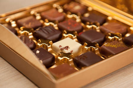 Golden box of handmade square shaped chocolates in different colors and types.の写真素材