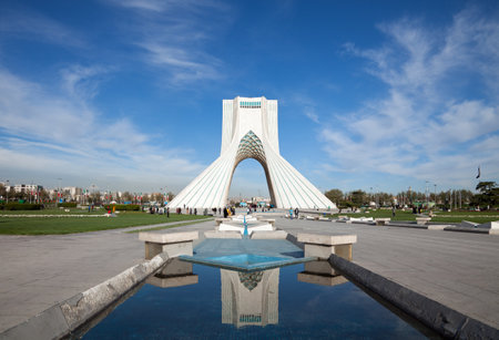 Azadi monument and its reflection on waterways in Azadi square of Tehran, against blue sky and white clouds.のeditorial素材