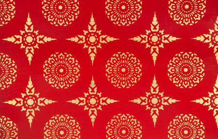 Ancient Thai painting with golden ink on red wall with a design consisting of stars and round circular flower shapes.の写真素材