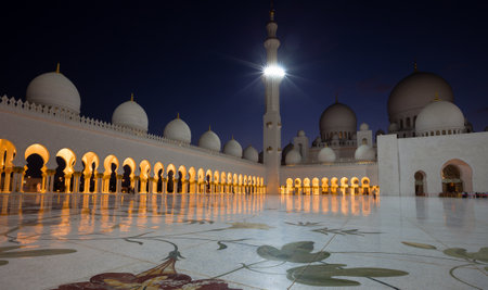 Arches of Sheikh Zayed Mosque illuminated with warm orange lights and reflected on white marble floor which is decorated with floral pattern.のeditorial素材